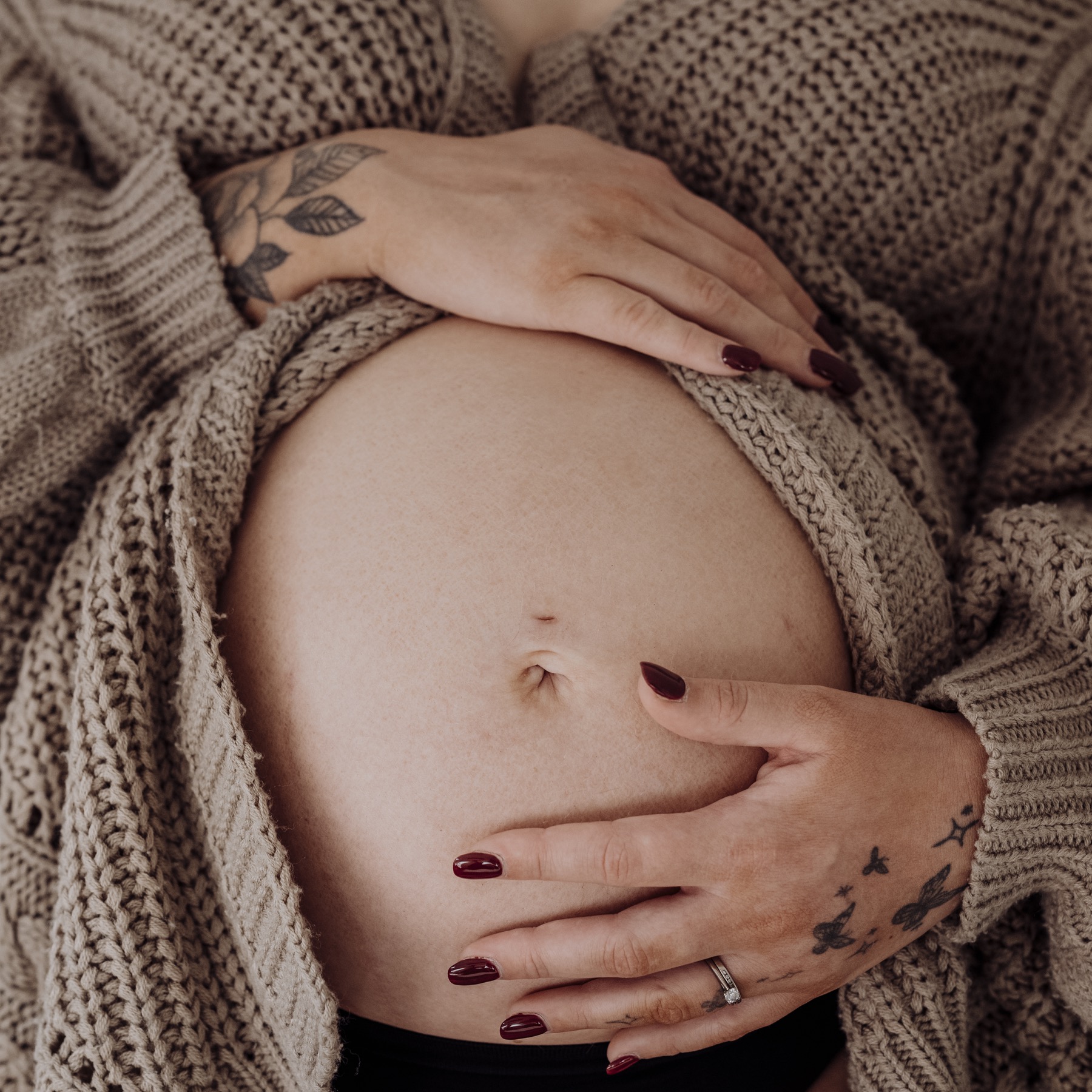 Hands cradling a baby bump surrounded by a knitted cardigan