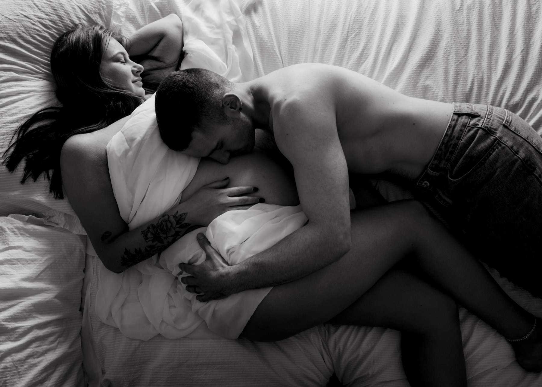 Black and white maternity portrait of a couple resting together on a bed
