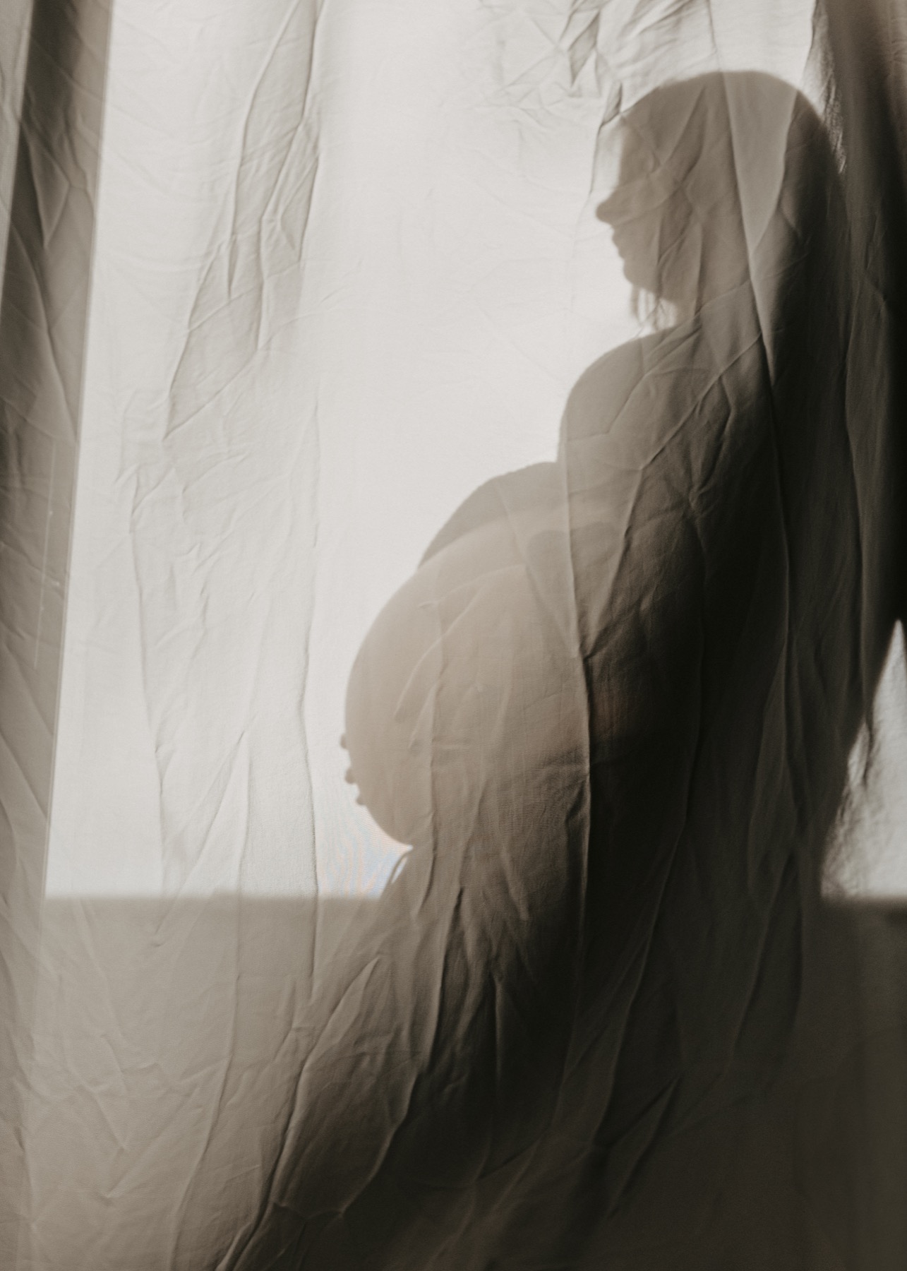 An expectant mother silhouetted behind a softly lit curtain