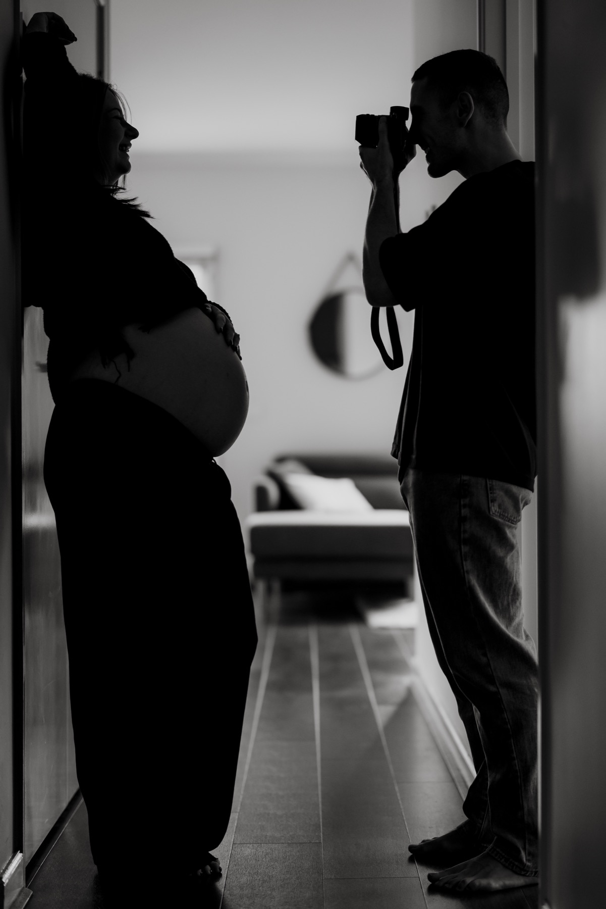 Silhouette of a partner photographing an expectant mother in a doorway
