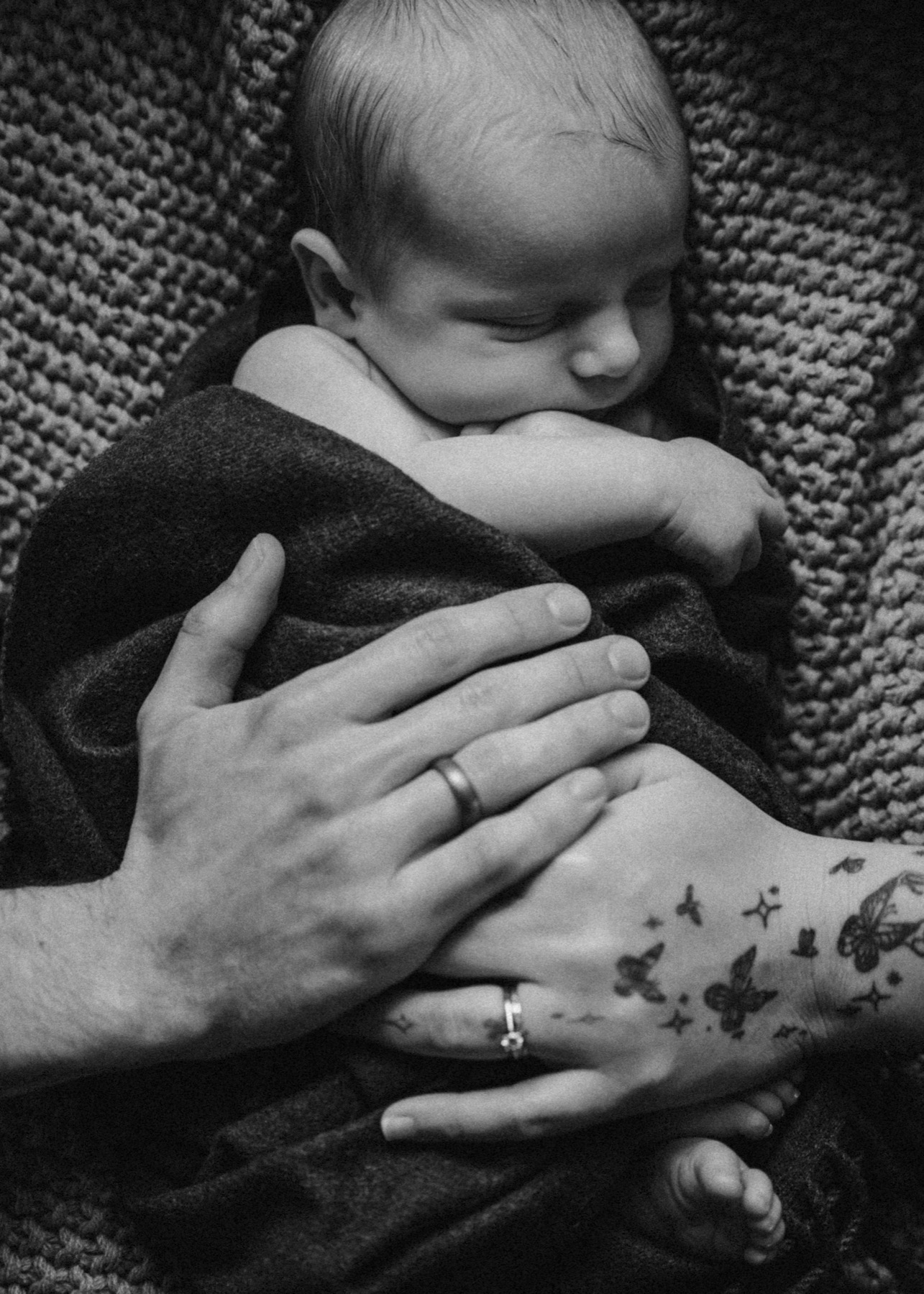 Sleeping newborn nestled in a blanket with parents hands resting together