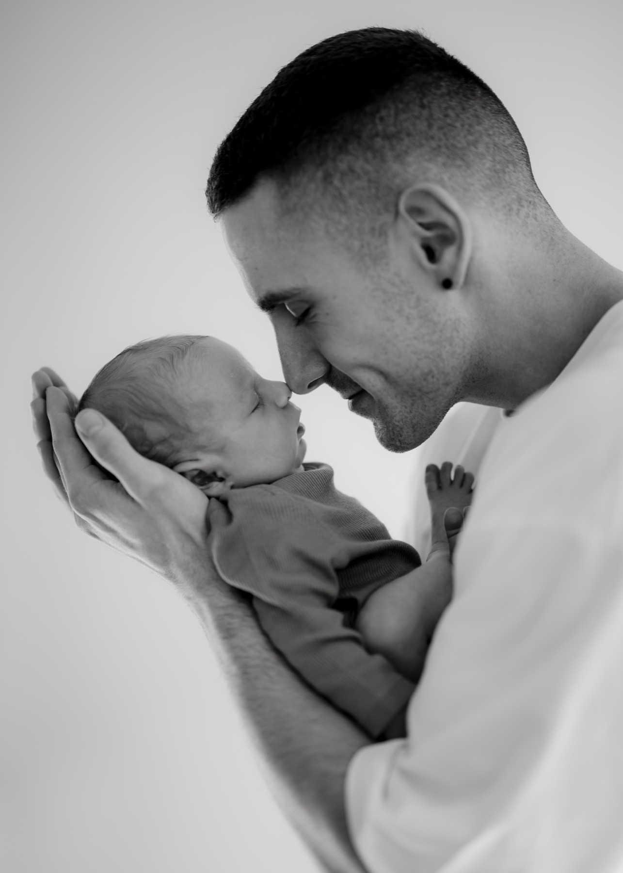 Black and white portrait of a father touching noses with his newborn