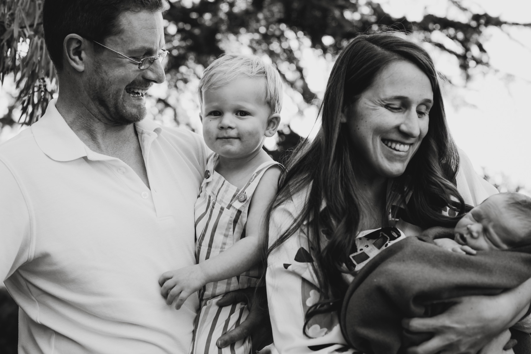 Black and white outdoor portrait of parents with their toddler and newborn