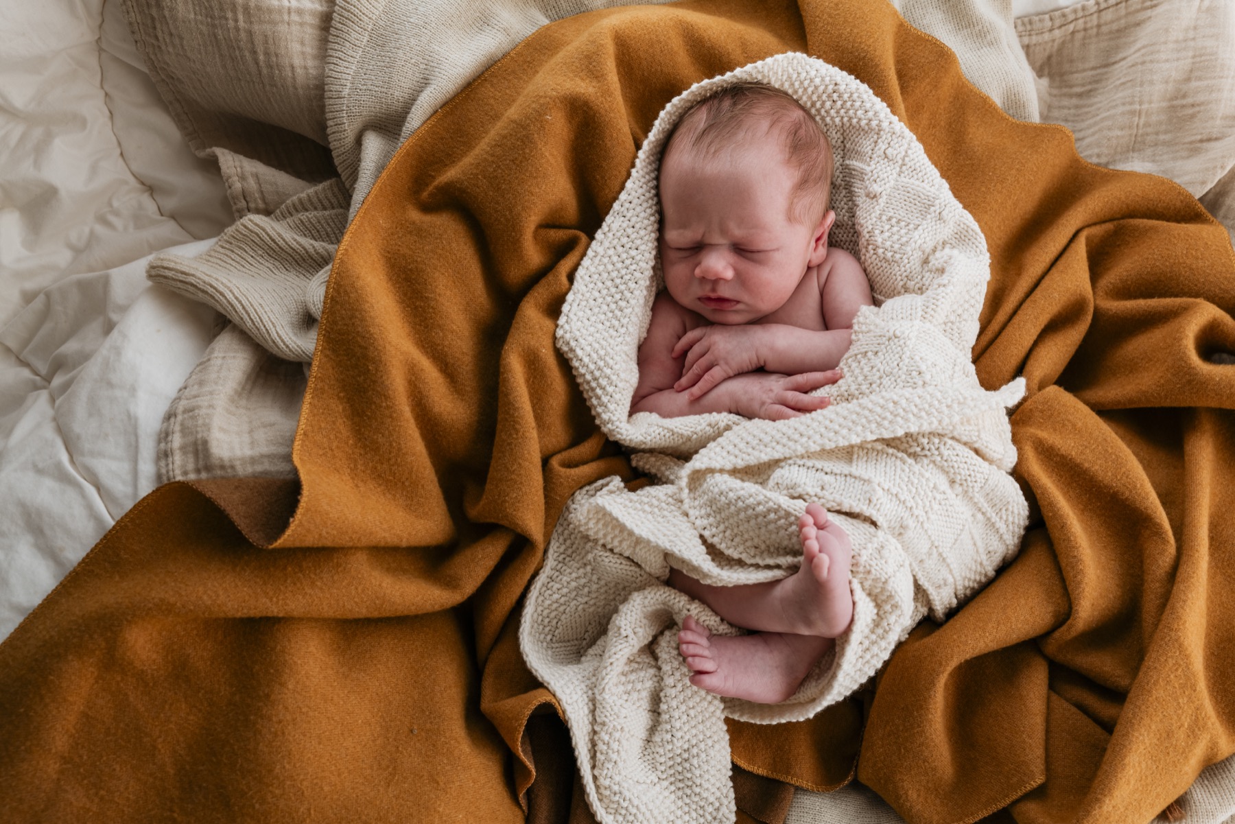 Newborn wrapped in a cream blanket on warm ochre bedding