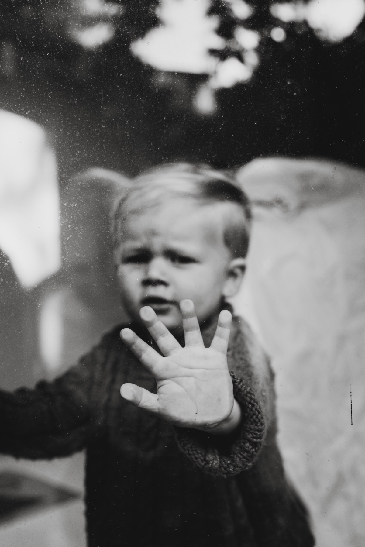 Black and white portrait of a child with a hand against window glass
