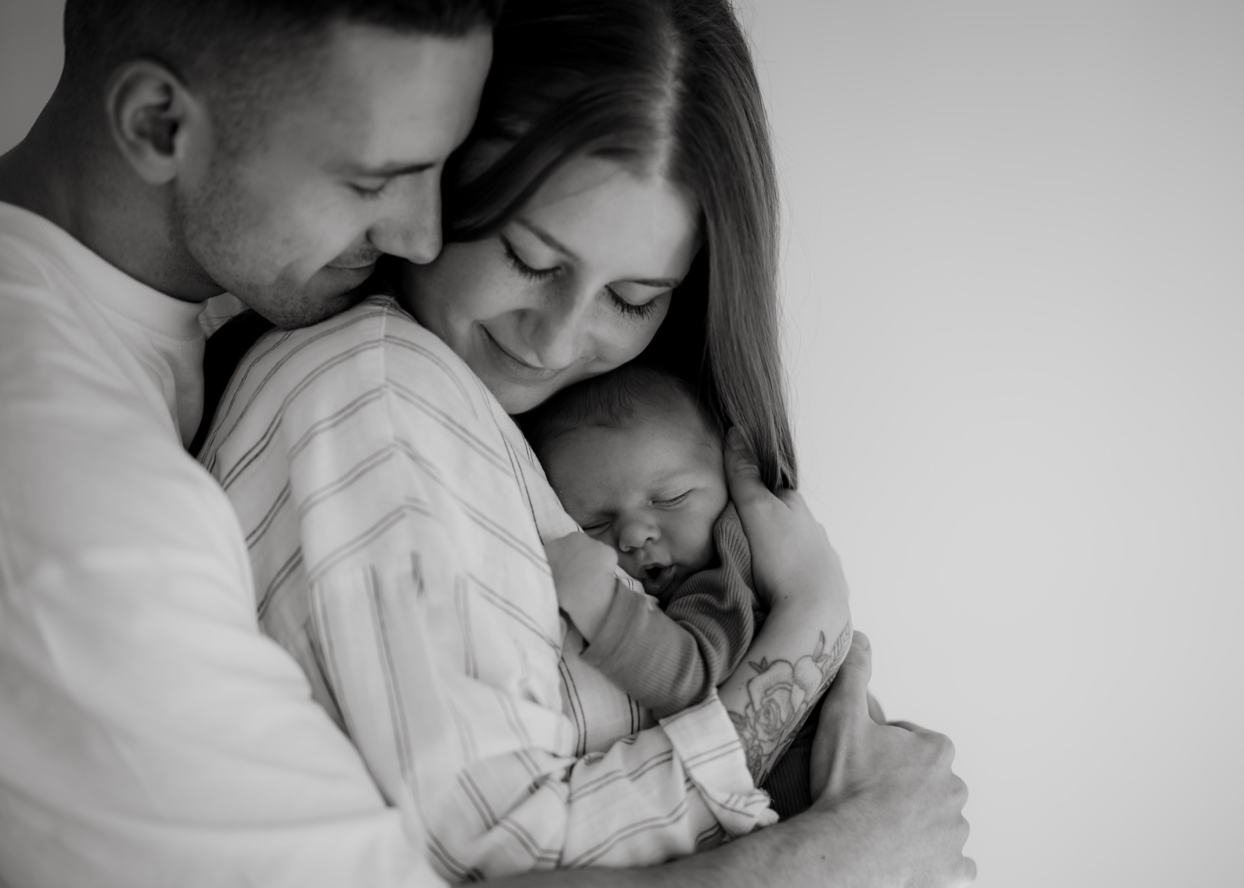 Black and white portrait of parents embracing their sleeping newborn