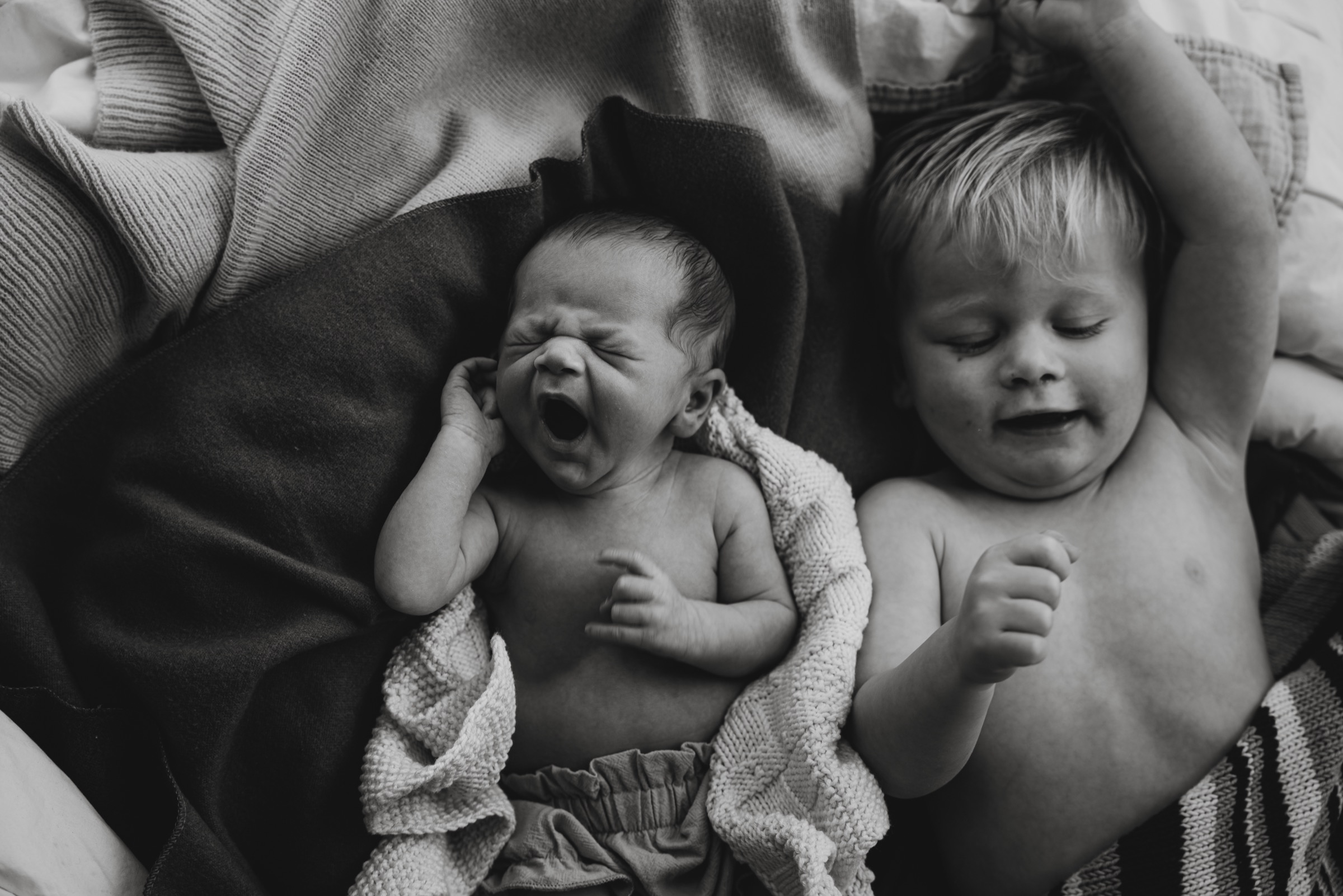 Black and white photograph of a yawning newborn beside an older sibling