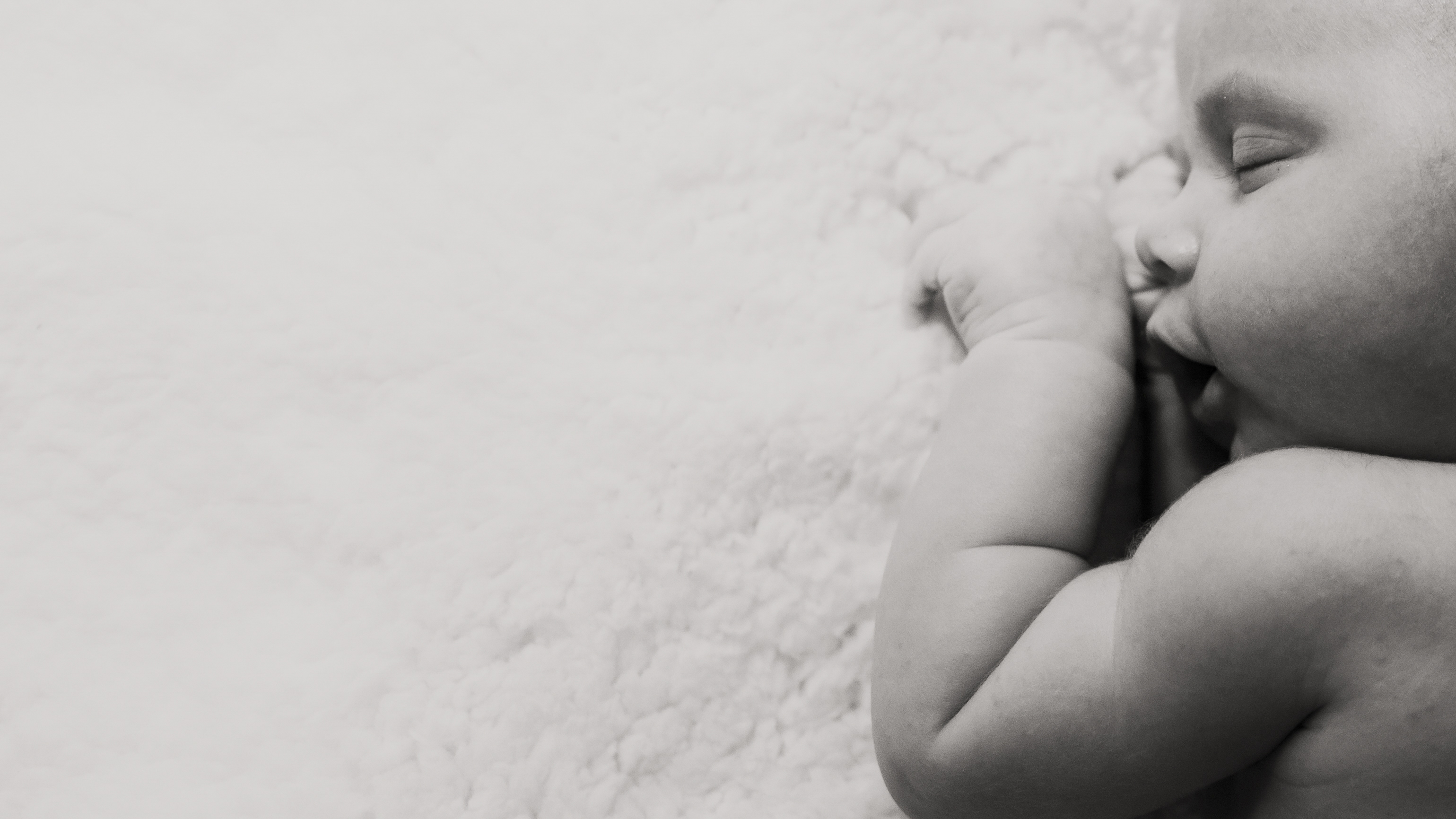 Black and white portrait of a sleeping newborn with a hand resting beside their face
